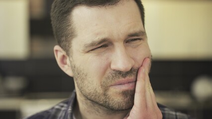 Sad handsome bearded male suffering from toothache while sitting at home