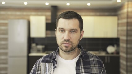 Obraz premium Young man drinking water to quench his thirst, standing at the kitchen at home