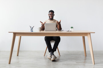 Fototapeta premium Handsome millennial black man sits at a desk in his home office, engaged in a video call. He uses a laptop and gestures while communicating from a comfortable workspace.