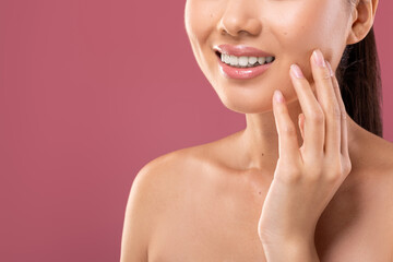 Fototapeta premium Unrecognizable young lady touches her face while showing off a perfect white smile against a purple background. This cropped shot highlights the importance of dental care and oral hygiene.