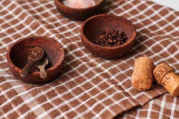 Rustic wooden bowls filled with spices and corks on a checkered cloth, showcasing culinary elements and natural textures in a cozy kitchen setting