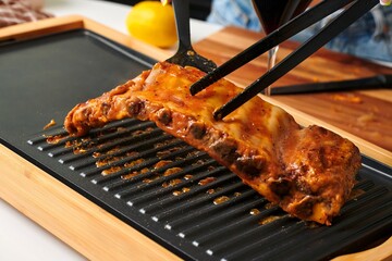 Grilled barbecue ribs being lifted with tongs from a sizzling grill, showcasing delicious glaze and juicy texture, perfect for culinary enthusiasts and food photography