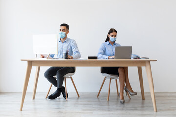 Diverse colleagues, a man and a woman, are working at their desks in a modern office.