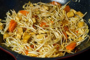 Close-up of a European-style adapted Asian stir-fry with tofu, bean sprouts, and carrots, cooking in a non-stick wok during home preparation