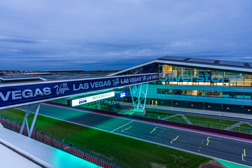 Naklejka premium The Silverstone pit building lit up at twilight, ideal for motorsport, travel, and architecture themes.
