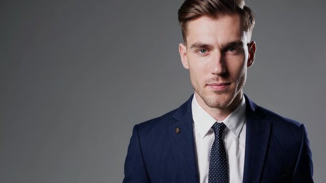 Confident young man in stylish suit poses for professional portrait against simple gray background