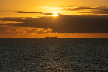 Cargo ship sailing at sunset near the horizon with golden light reflecting on the water surface