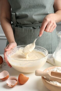 Woman making batter (liquid dough) at white table indoors, closeup