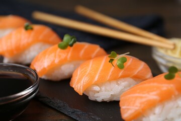 Delicious nigiri sushi with salmon, microgreens and soy sauce on wooden table, closeup