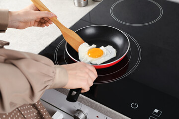 Woman taking fried egg with wooden spatula in kitchen, closeup