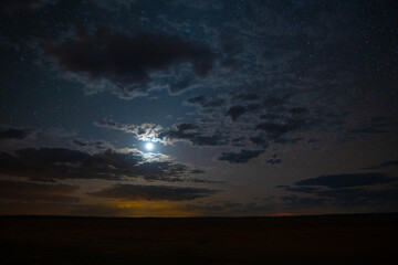 The moon and stars shining through clouds over a prairie