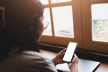 Over the shoulder view of a woman holding a smartphone with a blank white screen. A mockup for an...