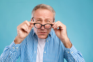 A senior man squints while wearing eyeglasses, struggling with vision issues. He appears focused...