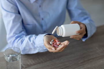 A young Indian woman sits at her workspace pouring various pills into her hand from a bottle. She is focused on managing her medications. This scene highlights the importance of treatment and health.