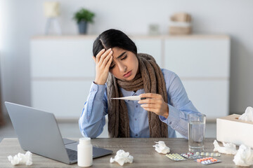 In an office setting, a sad young hindu woman manager sits by her computer looking distressed. She...