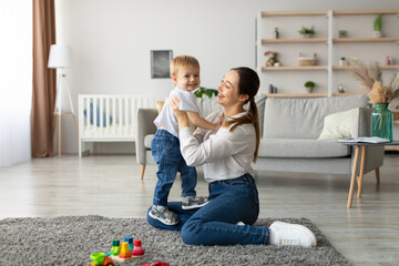 A joyful mother and her smiling son engage in fun playtime in a spacious living room. The child...