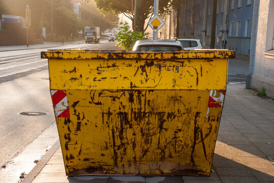Dirty Yellow Construction Dumpster at Sunrise on Munich City Sidewalk