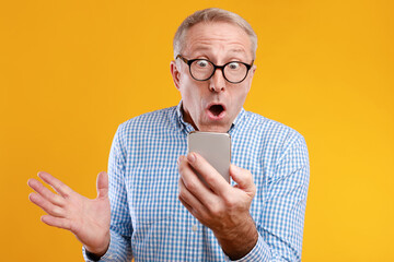 Mature man in glasses shows excitement while reading surprising information on his smartphone....