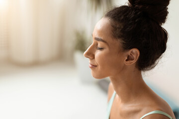 A young brunette woman stands indoors, eyes closed and smiling gently. © Prostock-studio