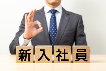 Obraz premium 「新入社員」と書かれたブロックとOKポーズをするビジネスマン