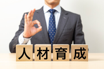 Obraz premium 「人材育成」と書かれたブロックとOKポーズをするビジネスマン