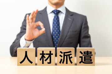 「人材派遣」と書かれたブロックとOKポーズをするビジネスマン