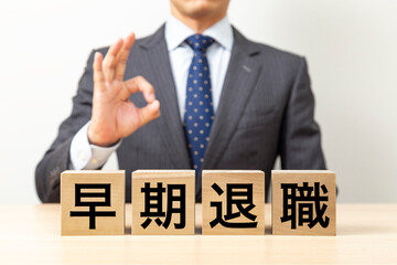 「早期退職」と書かれたブロックとOKポーズをするビジネスマン