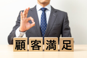 「顧客満足」と書かれたブロックとOKポーズをするビジネスマン