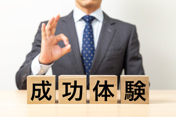 「成功体験」と書かれたブロックとOKポーズをするビジネスマン
