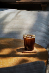 a glass of iced americano coffee on wooden table in sun light and shade