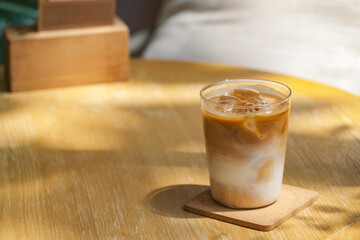 a glass of iced milk coffee on wooden table in sun light and shade
