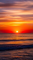 Obraz premium Vibrant ocean waves meet a fiery sunset sky with a bright sun low on the horizon
