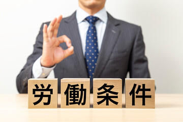 Obraz premium 「労働条件」と書かれたブロックとOKポーズをするビジネスマン