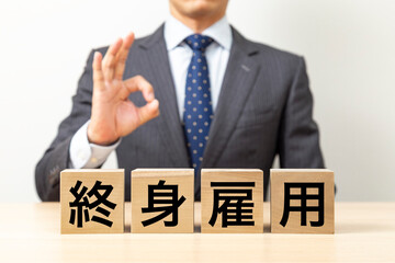 Obraz premium 「終身雇用」と書かれたブロックとOKポーズをするビジネスマン