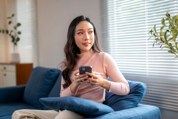 Young woman using smartphone and relaxing on sofa at home
