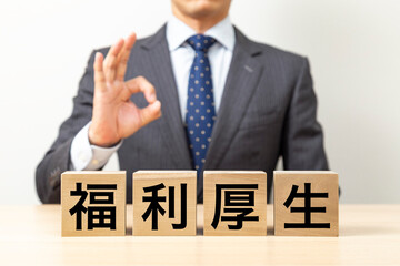 「福利厚生」と書かれたブロックとOKポーズをするビジネスマン