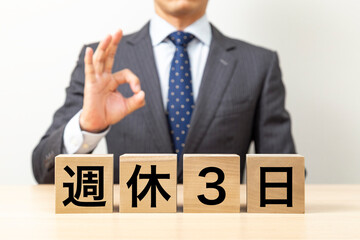 「週休3日」と書かれたブロックとOKポーズをするビジネスマン