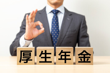 Obraz premium 「厚生年金」と書かれたブロックとOKポーズをするビジネスマン