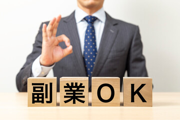 「副業OK」と書かれたブロックとOKポーズをするビジネスマン