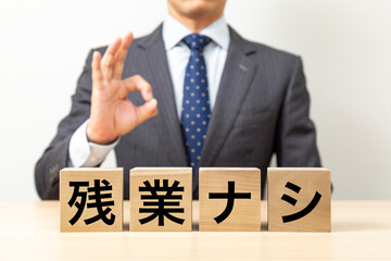 「残業ナシ」と書かれたブロックとOKポーズをするビジネスマン