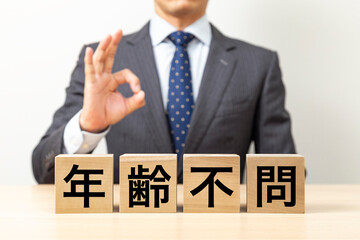 「年齢不問」と書かれたブロックとOKポーズをするビジネスマン