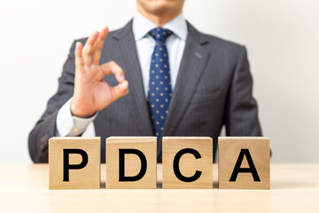 「PDCA」と書かれたブロックとOKポーズをするビジネスマン