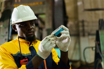 African engineer inspecting metal part from machine for quality and precision.