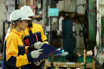 Male and female engineers reviewing machinery maintenance documents in factory.