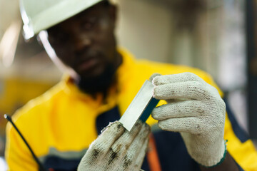 African engineer inspecting metal part from machine for quality and precision.