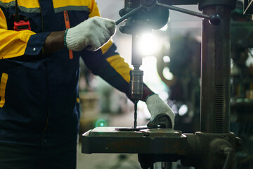 African American male metal worker operating drill press machine.