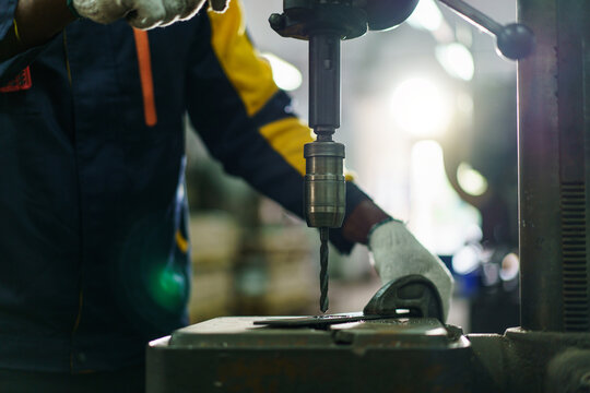 African American male metal worker operating drill press machine.