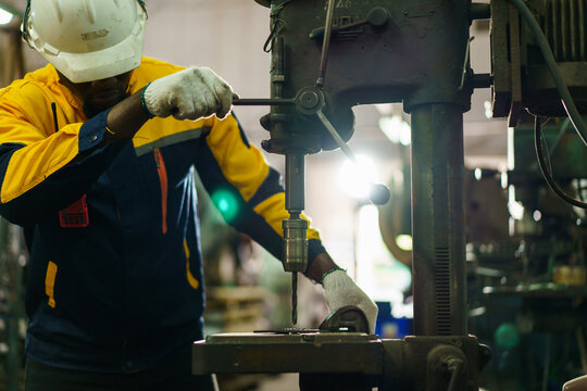 African American male metal worker operating drill press machine. - Powered by Adobe