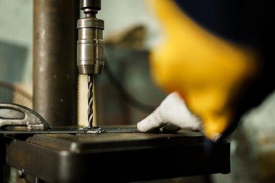 African American male metal worker operating drill press machine.