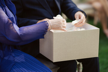 Elegant hands picking delicate petals from a textured beige box during a wedding ceremony. A quiet,...